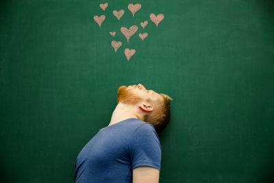 Young man looking at heart shape drawing on blackboard