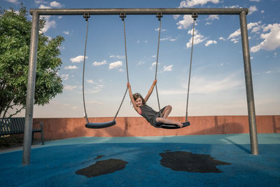 Young girl plays on a swing holding another swing at a playground