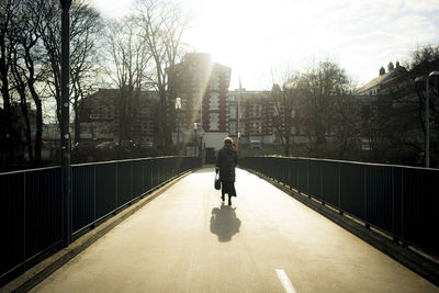 Rear view of man walking on bridge in city