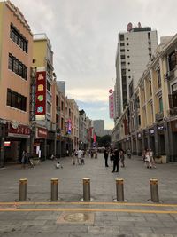 People walking on street amidst buildings in city against sky