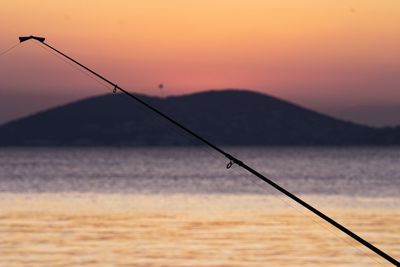 Fishing rod by sea against sky during sunset