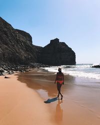 Rear view of bikini woman walking at beach against clear sky