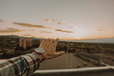 Cropped hand of man gesturing against sky during sunset