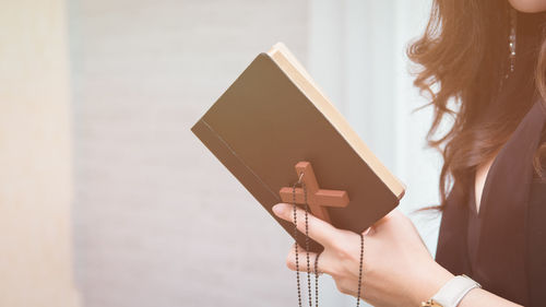 Midsection of woman holding bible and rosary