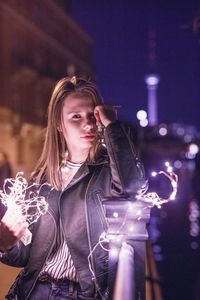 Young woman with illuminated string lights in city at night