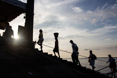 Silhouette people standing by sea against sky during sunset