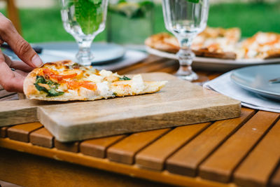 Cropped hand holding pizza slice on cutting board