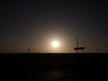 Silhouette electricity pylons on land against sky during sunset