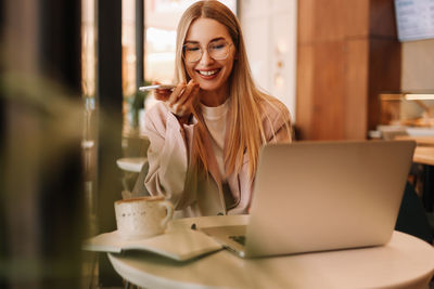 A female millennial student records a voice message and studies online using a laptop and smartphone