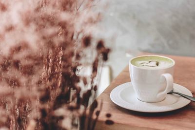 Close up green tea latte art in white cup on wooden table at cafe