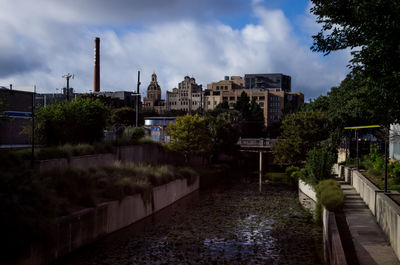 View of buildings by river against cloudy sky