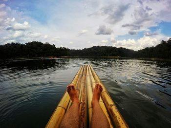 Low section of man on bamboo raft in lake against sky