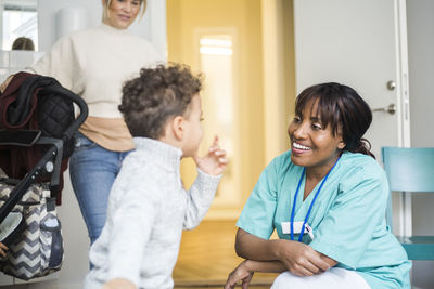 Boy talking to smiling female nurse while mother standing in background at medical clinic