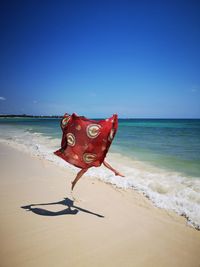 Woman holding textile jumping at beach against sky