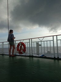 Rear view of man standing by railing against sea