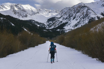 Rear view of hiker splitboarding on snow covered land against mountains