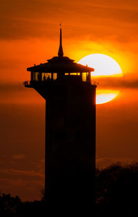 Silhouette lighthouse by sea against orange sky