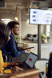 Smiling businessman and businesswoman sitting with technologies during meeting at office