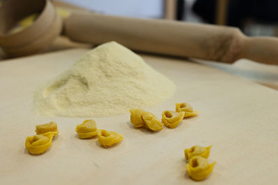 Freshly made raw tortellini over wooden table and a rolling pin and flour in the background.