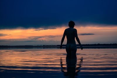 Rear view of naked woman standing in lake against cloudy sky