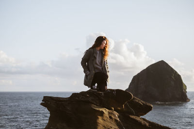 Woman standing on rock by sea against sky