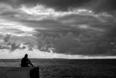 Rear view of man looking at sea against cloudy sky