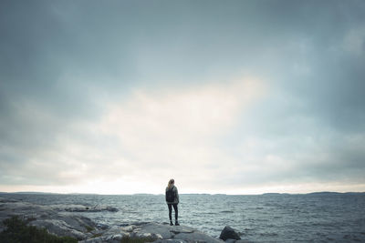 Rear view of wonderlust woman standing on rock by sea against cloudy sky