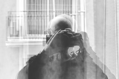 Portrait of man photographing through window at home