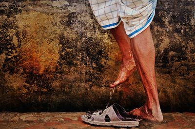 Low section of man with wet feet standing against weathered wall