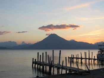 Wooden posts in sea against sky during sunset