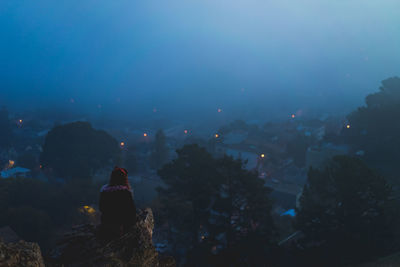 Rear view of people sitting on rock against sky at night