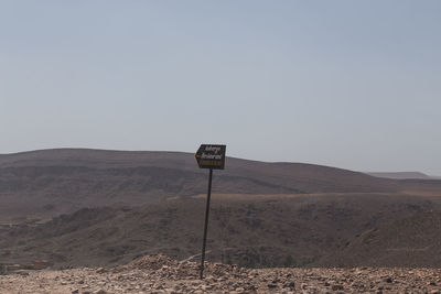 Sign board on desert against clear sky