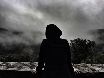 Rear view of silhouette man standing by wall during foggy weather