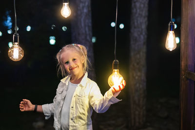 Portrait of smiling girl holding illuminated lights at night