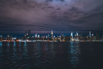 Illuminated buildings by sea against sky at night