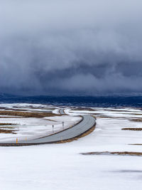 Road throught land covered in snow and ice with dark clouds in the background
