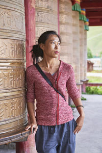 Young woman looking away while standing against built structure