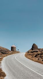 Empty road amidst land against clear blue sky