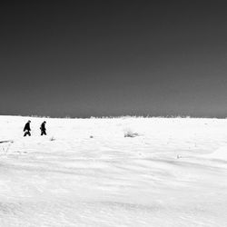 People walking on snow covered field against clear sky during winter