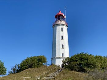 Lighthouse by trees against clear blue sky, hiddensee