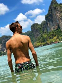 Rear view of shirtless man standing in river against sky