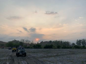 Cars on field against sky during sunset