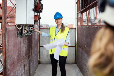 Construction manager holding documents while showing machinery in construction elevator