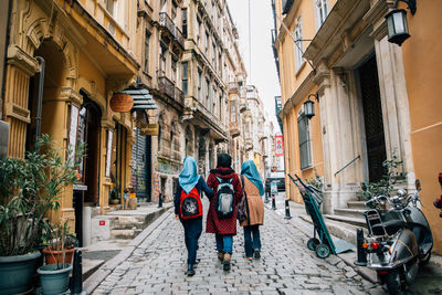 Rear view of women in hijab and backpack walking on street amidst building