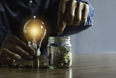 Midsection of man holding illuminated light bulb on table