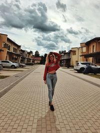 Full length portrait of young woman in city against sky