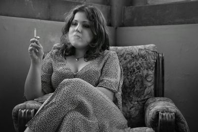 Thoughtful young woman smoking cigarette while sitting on chair
