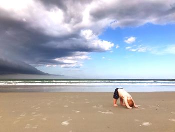 Baby boy bending on beach against sky