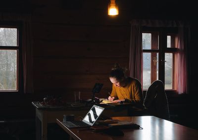 Young woman drawing on paper while sitting in cottage