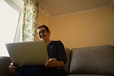 Smiling senior woman sitting at home office workplace looking in laptop.